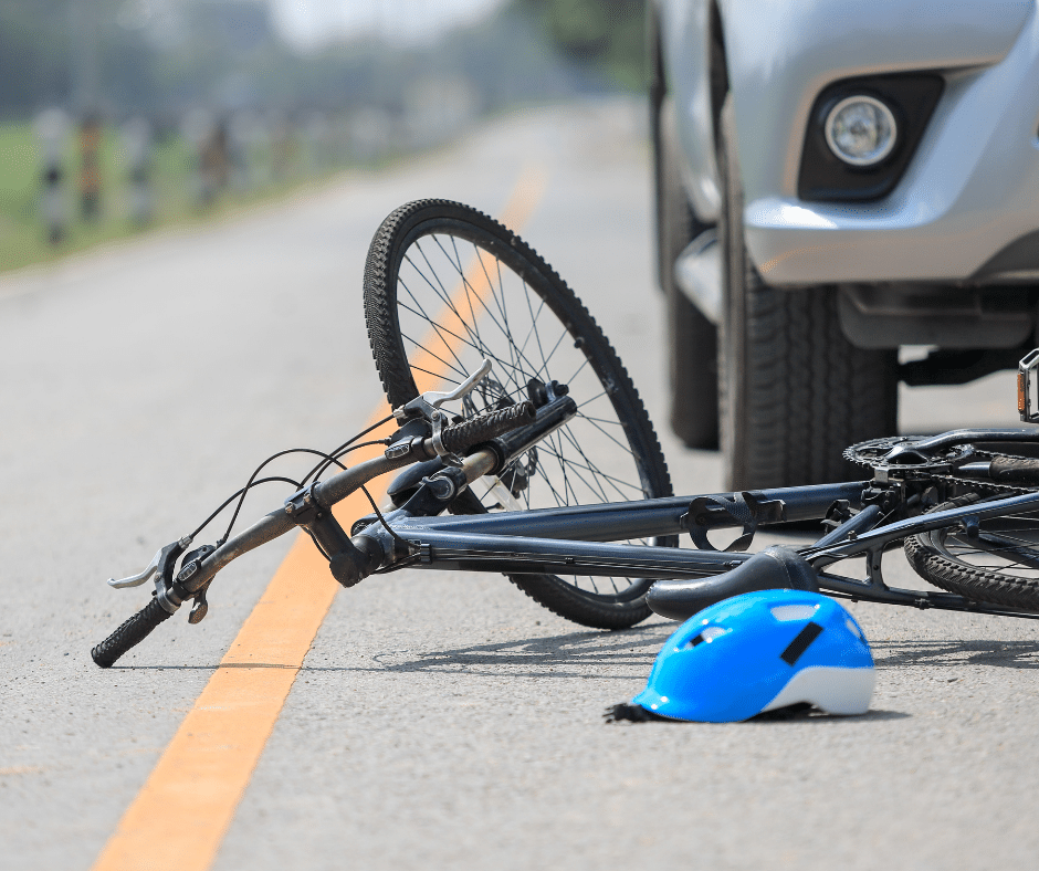 A bike and helmet on the road with a car nearby, suggesting a bicycle accident, an area of legal expertise for Semenza Law.